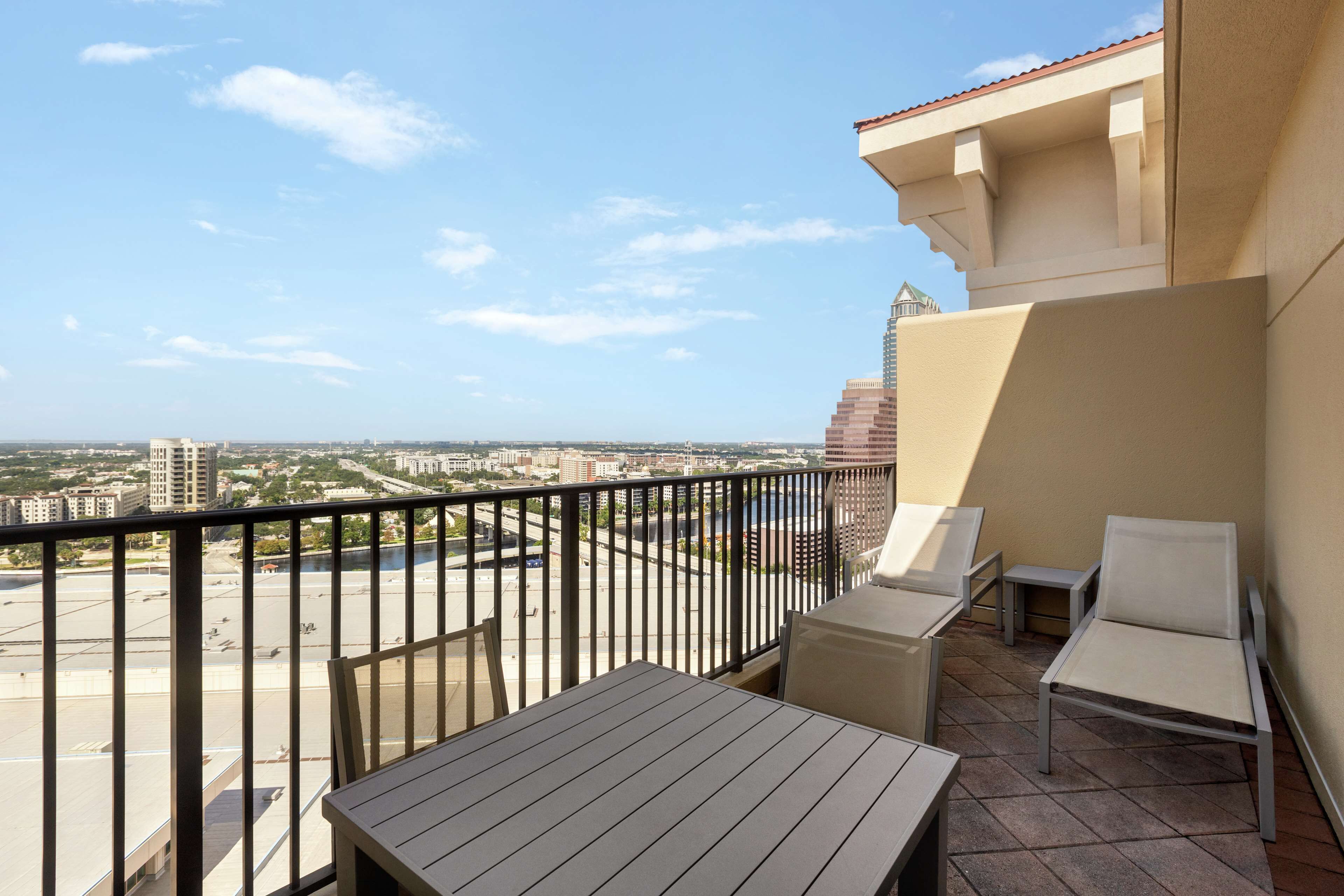 A balcony with a table and two chairs, overlooking a cityscape with buildings and a road.