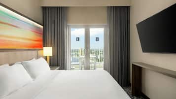 A hotel room with a large bed, a TV mounted on the wall, and a balcony with a city view.