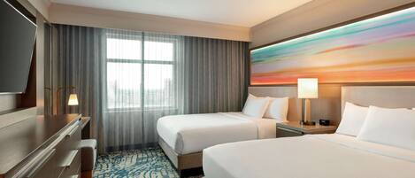 Habitación de hotel con dos camas, un escritorio, televisor y un ventanal con cortinas.