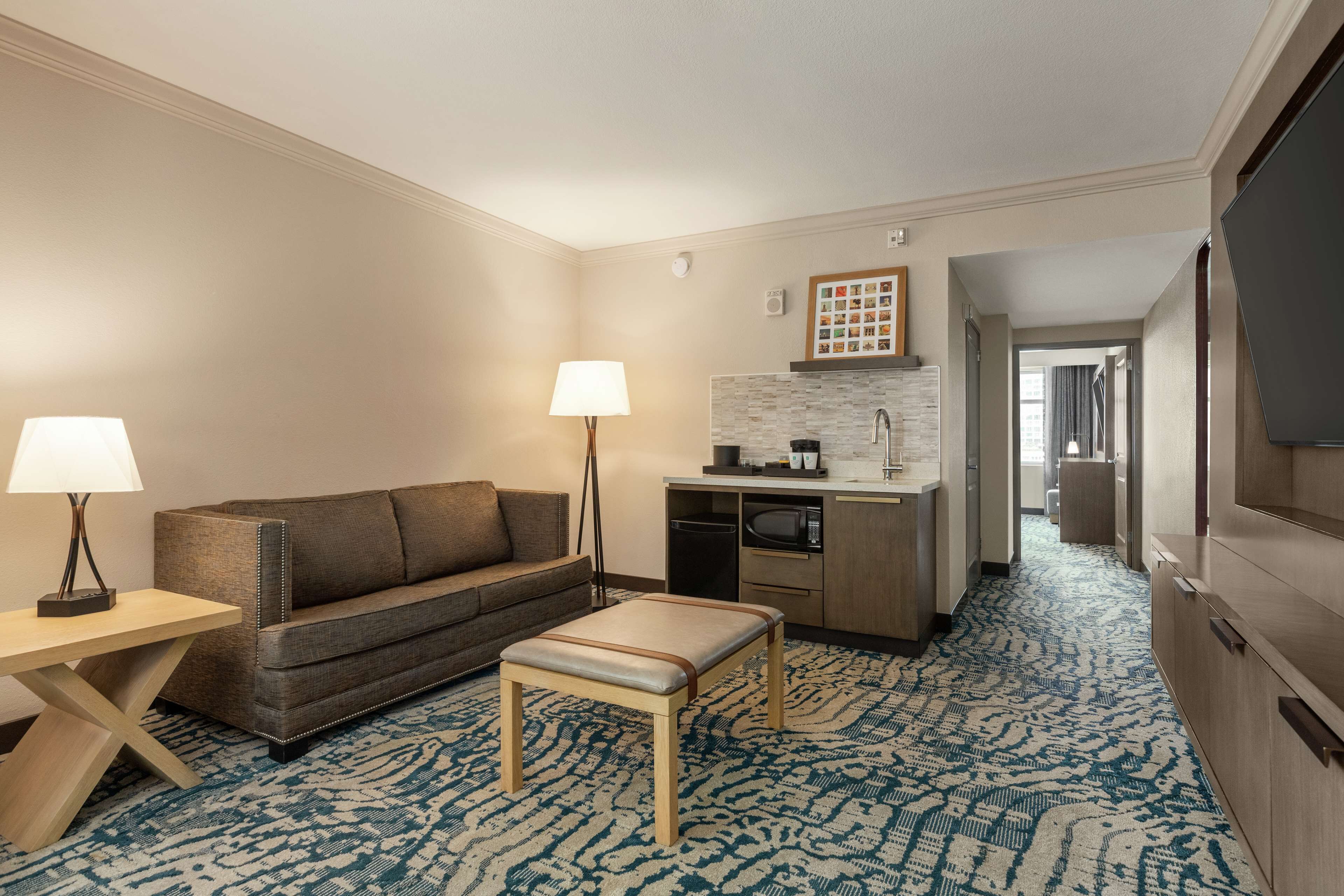 Ein Hotelzimmer mit Sofa, kleinem Tisch, Lampe, Küchenzeile und Fernseher.