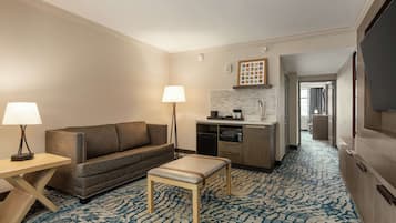 Ein Hotelzimmer mit Sofa, kleinem Tisch, Lampe, Küchenzeile und Fernseher.