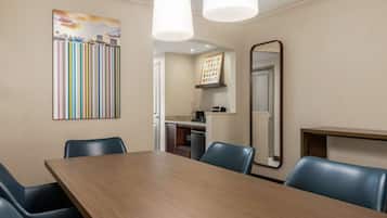 A conference room with a wooden table, blue chairs, a painting, a mirror, and a kitchenette in the background.