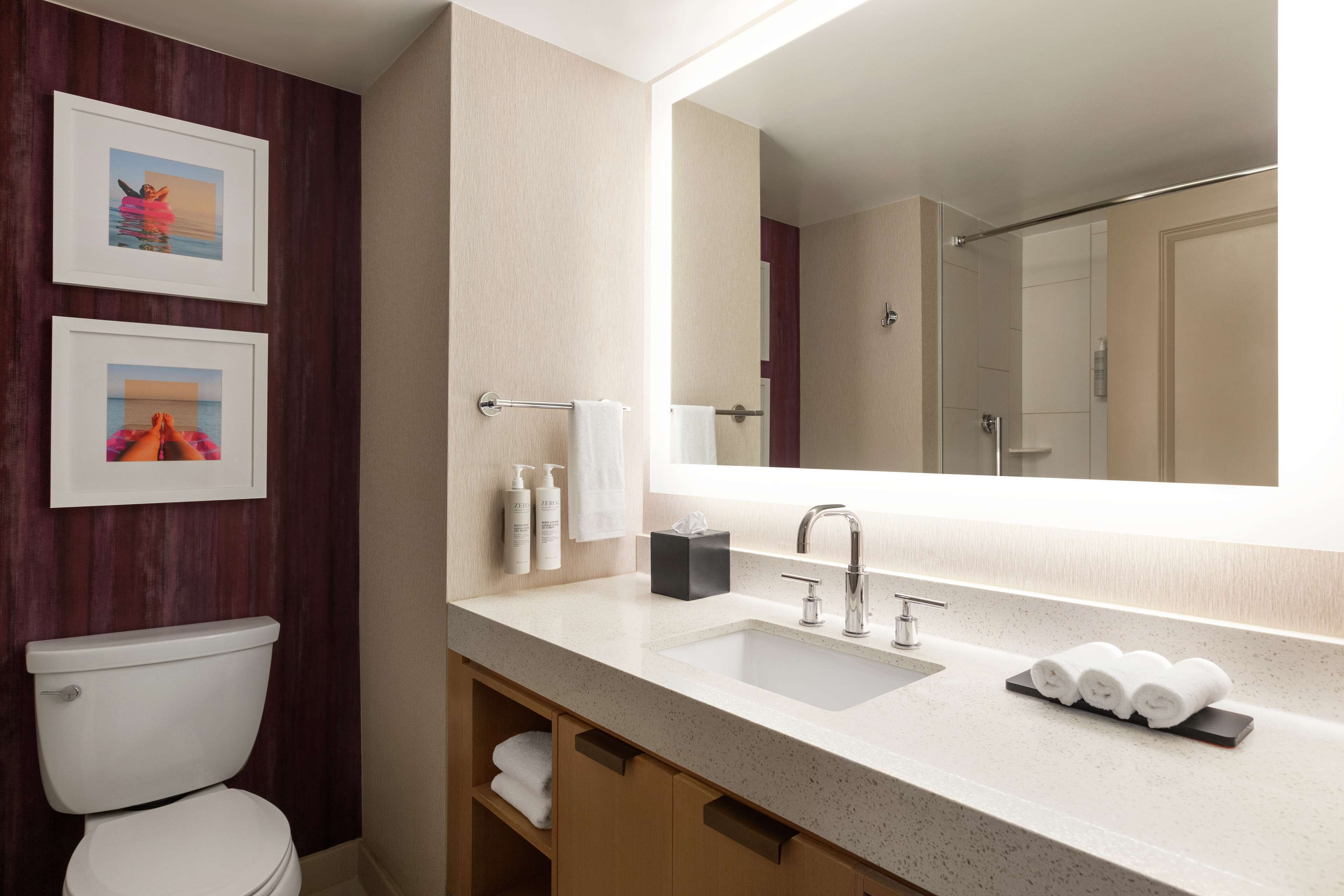 Ein modernes Badezimmer mit Toilette, großem Spiegel, Waschbecken und Handtuchhalter sowie gerahmten Bildern an der Wand.