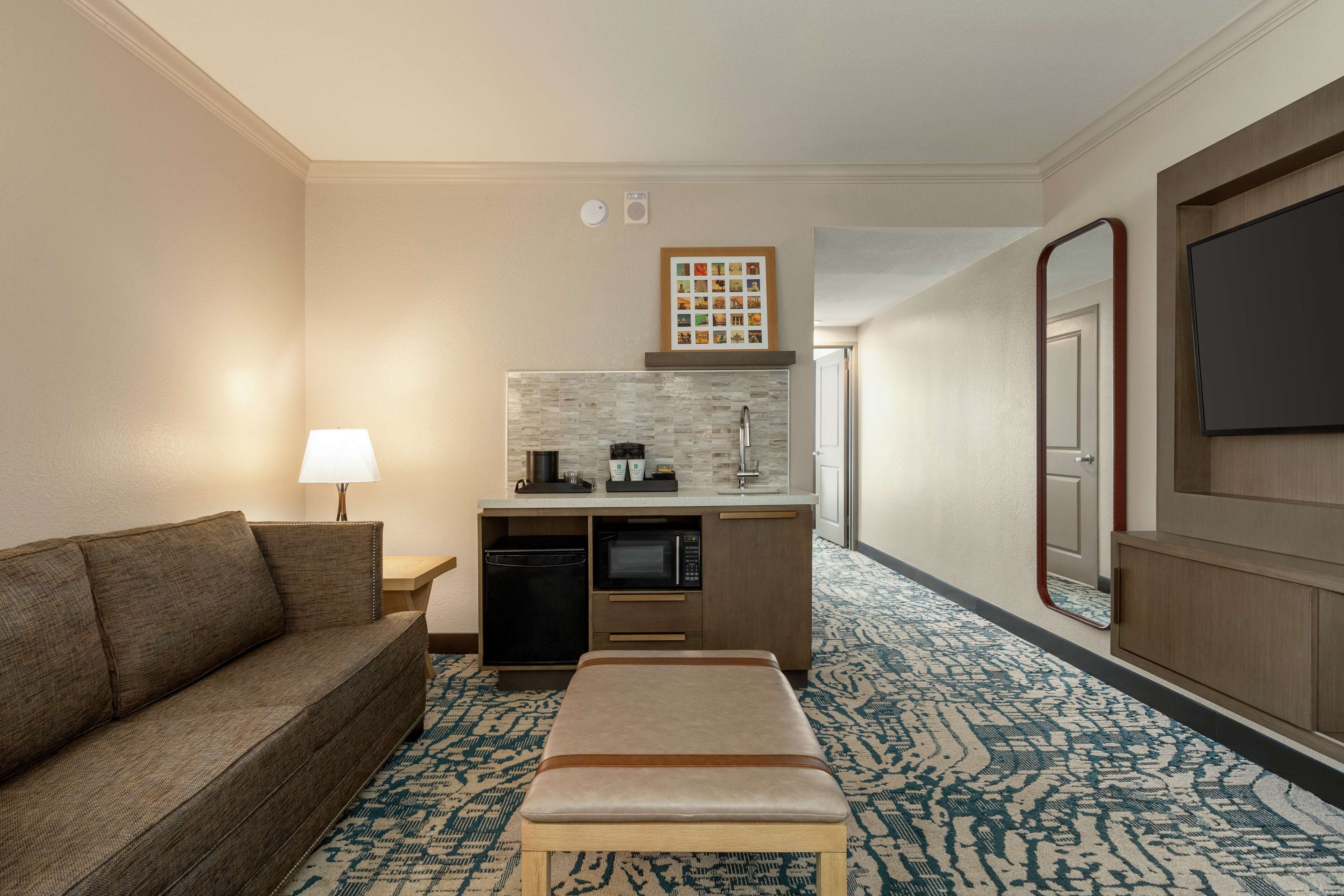 Habitación de hotel con sofá, kitchenette pequeña, televisión y alfombra estampada.