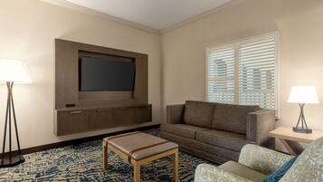A hotel room with a flat-screen TV mounted on the wall, a sofa, a patterned rug, and two floor lamps.