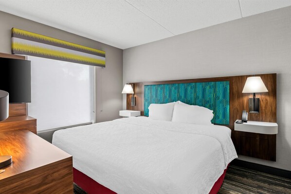 A hotel room with a large bed, a wooden desk, a television, and a wall-mounted lamp.