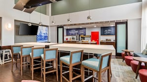 A modern bar area with a long counter, multiple bar stools, and a television screen. - Hampton Inn & Suites Richmond/Virginia Center (Glen Allen)