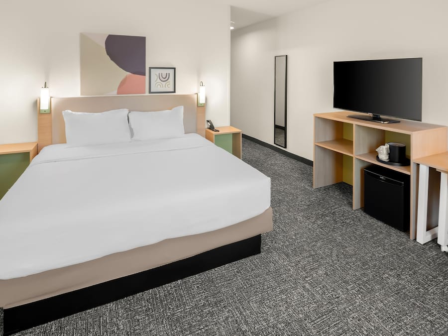 A hotel room with a bed, bedside tables, a desk with a chair, a television, and a large mirror.
