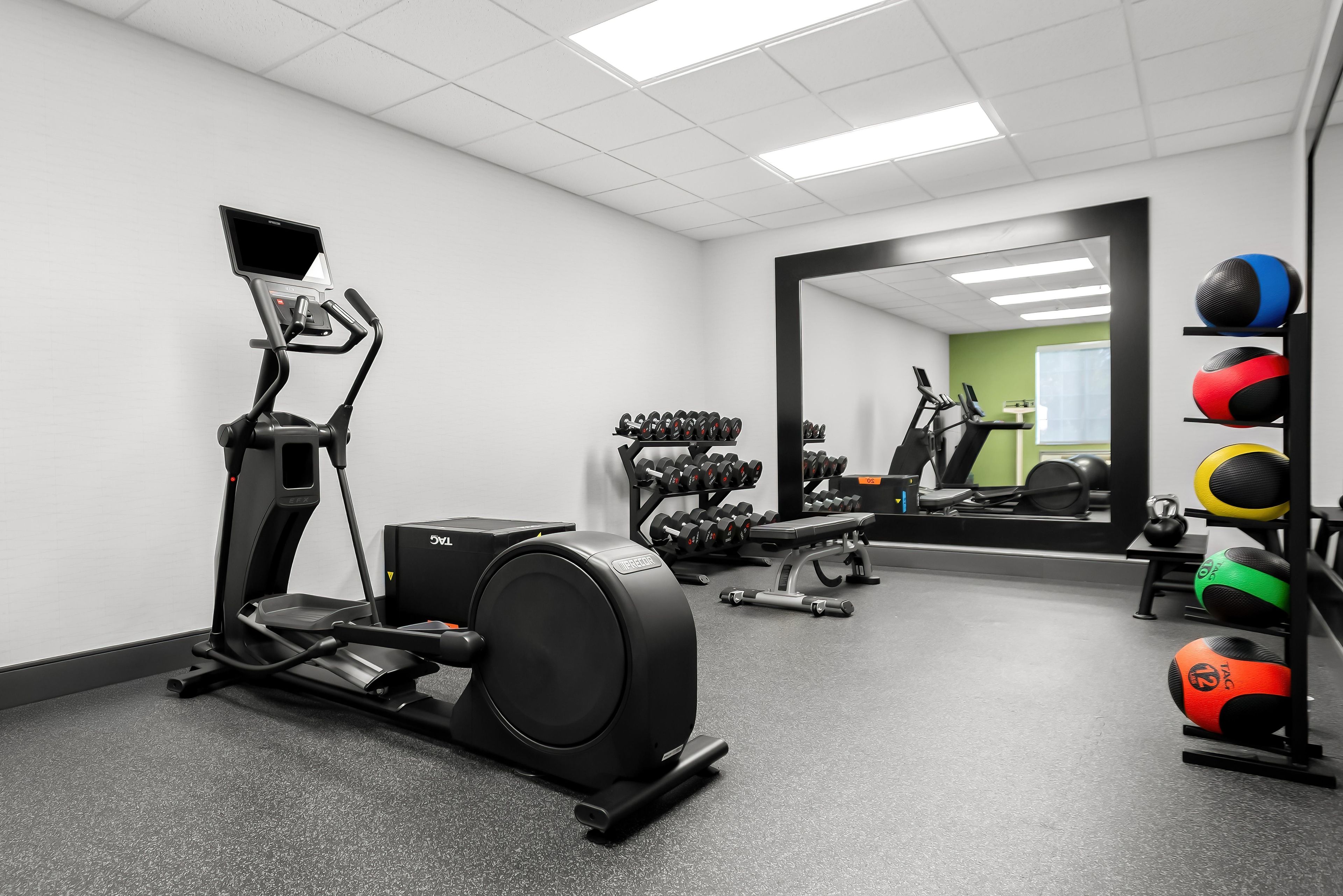A gym with exercise equipment, including a treadmill, weights, and a mirror reflecting the space.