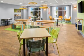 A modern indoor space with multiple tables and chairs, large windows, and a ceiling with recessed lighting. - Spark by Hilton Grand Island (Grand Island)