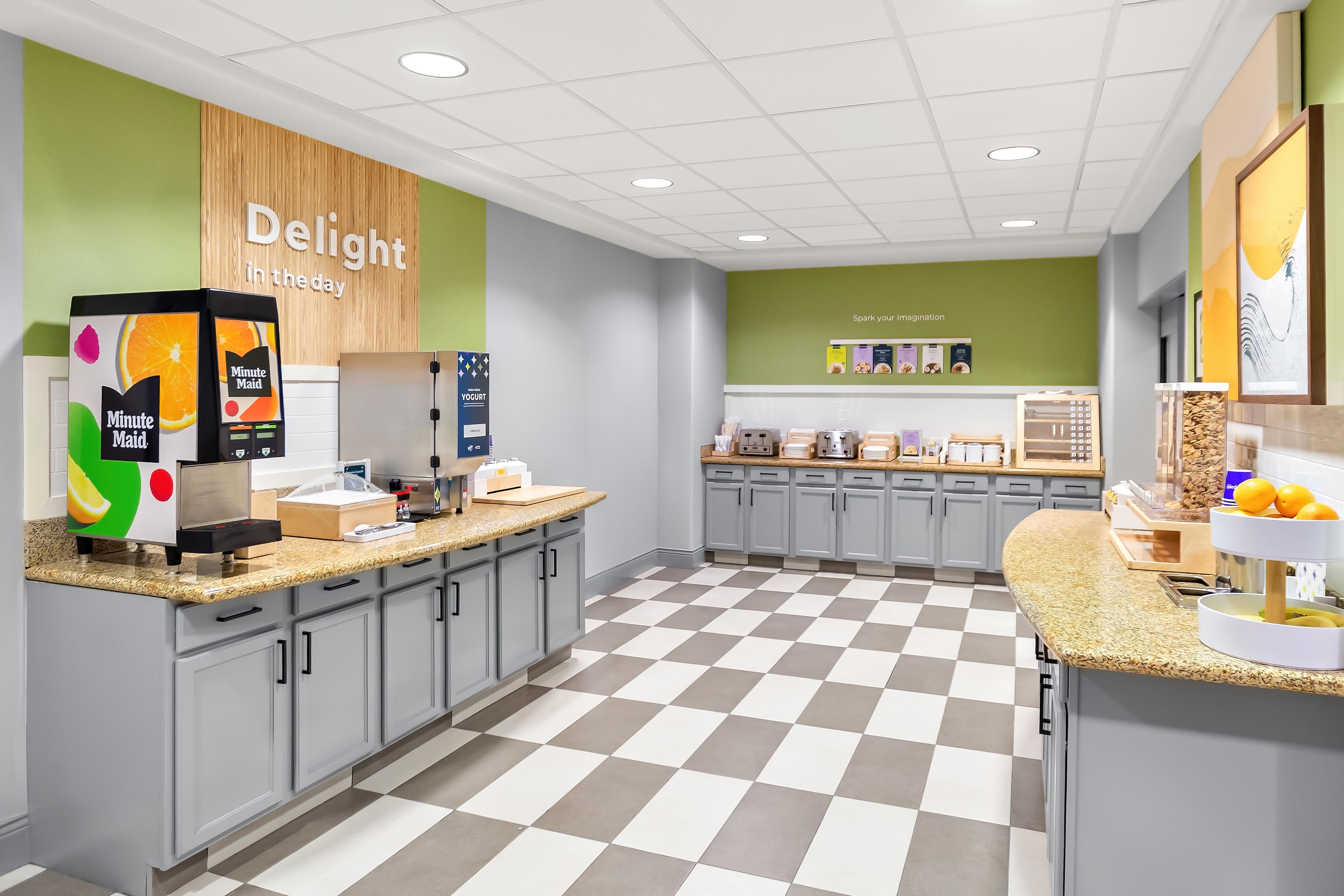 Een modern café met een zwart-wit geruit vloertje, een toonbank met een selectie Minute Maid-sapjes, en een muur met de tekst 'Delight in the day'.