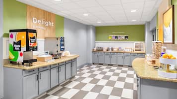 Een modern café met een zwart-wit geruit vloertje, een toonbank met een selectie Minute Maid-sapjes, en een muur met de tekst 'Delight in the day'.