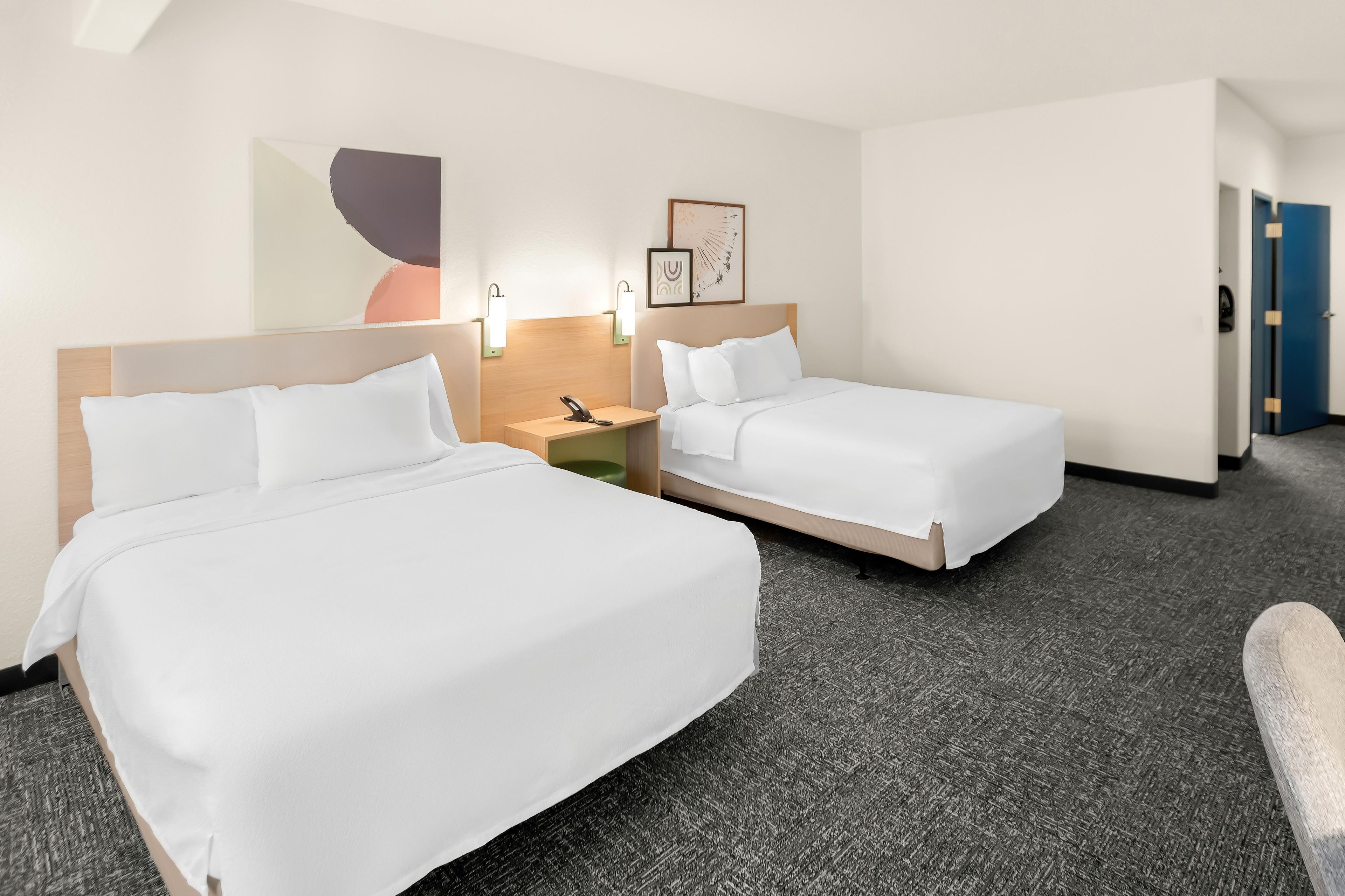 A hotel room with two single beds, a nightstand, a phone, and a wall-mounted light fixture.