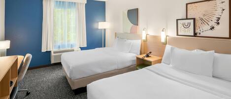A hotel room with two beds, a desk, a chair, a window with curtains, a wall-mounted phone, and a wall art piece.