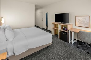 A hotel room with a bed, a desk, a television, a chair, and a small refrigerator.