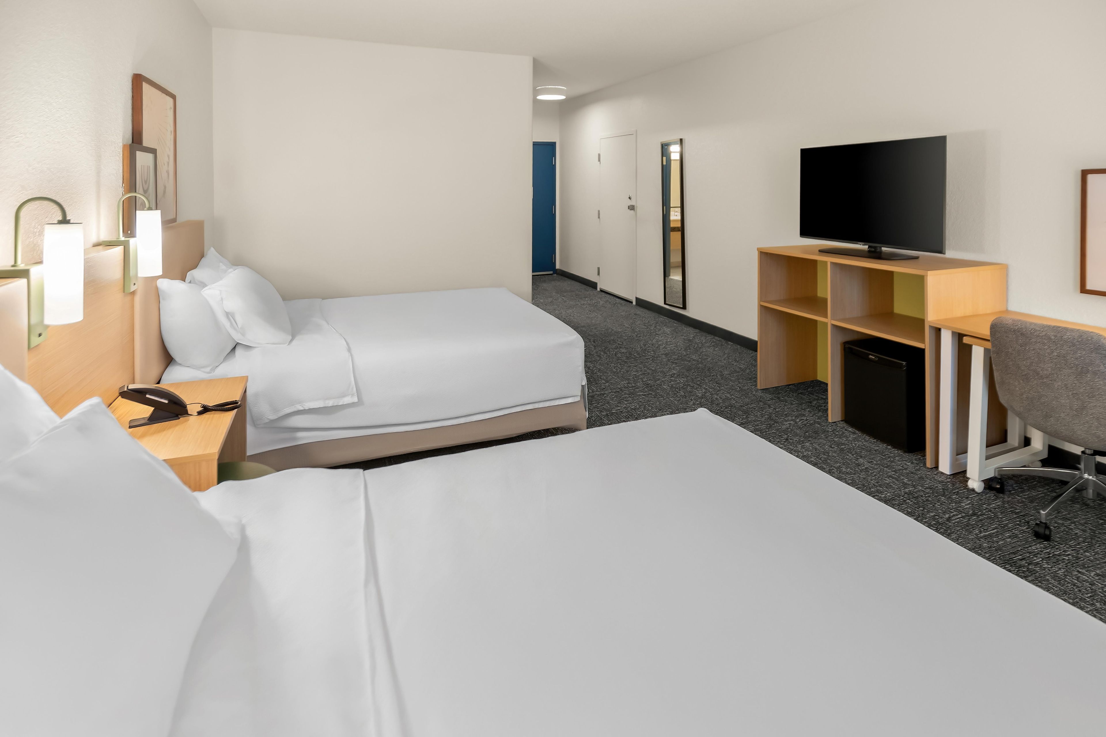 Habitación de hotel con dos camas, un escritorio con televisor y una pequeña zona de estar.
