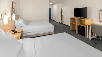 Habitación de hotel con dos camas, un escritorio con televisor y una pequeña zona de estar.