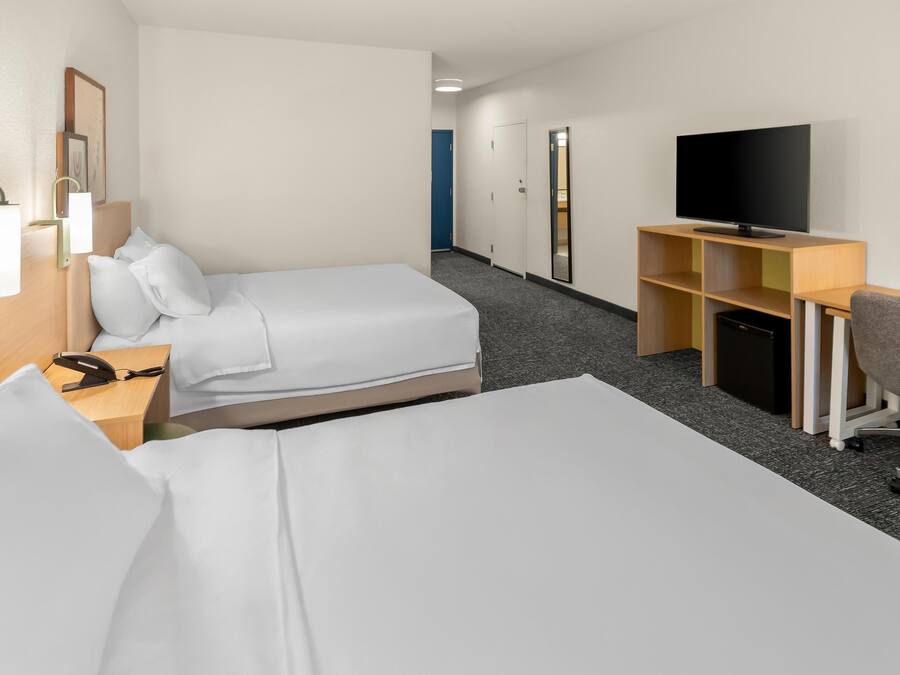 Quarto de hotel com duas camas, uma mesa de trabalho com televisão e uma pequena área de estar.