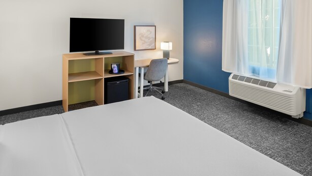 A hotel room with a bed, a desk, a chair, a television, a lamp, and a window with curtains. - Spark by Hilton Grand Island (Grand Island)