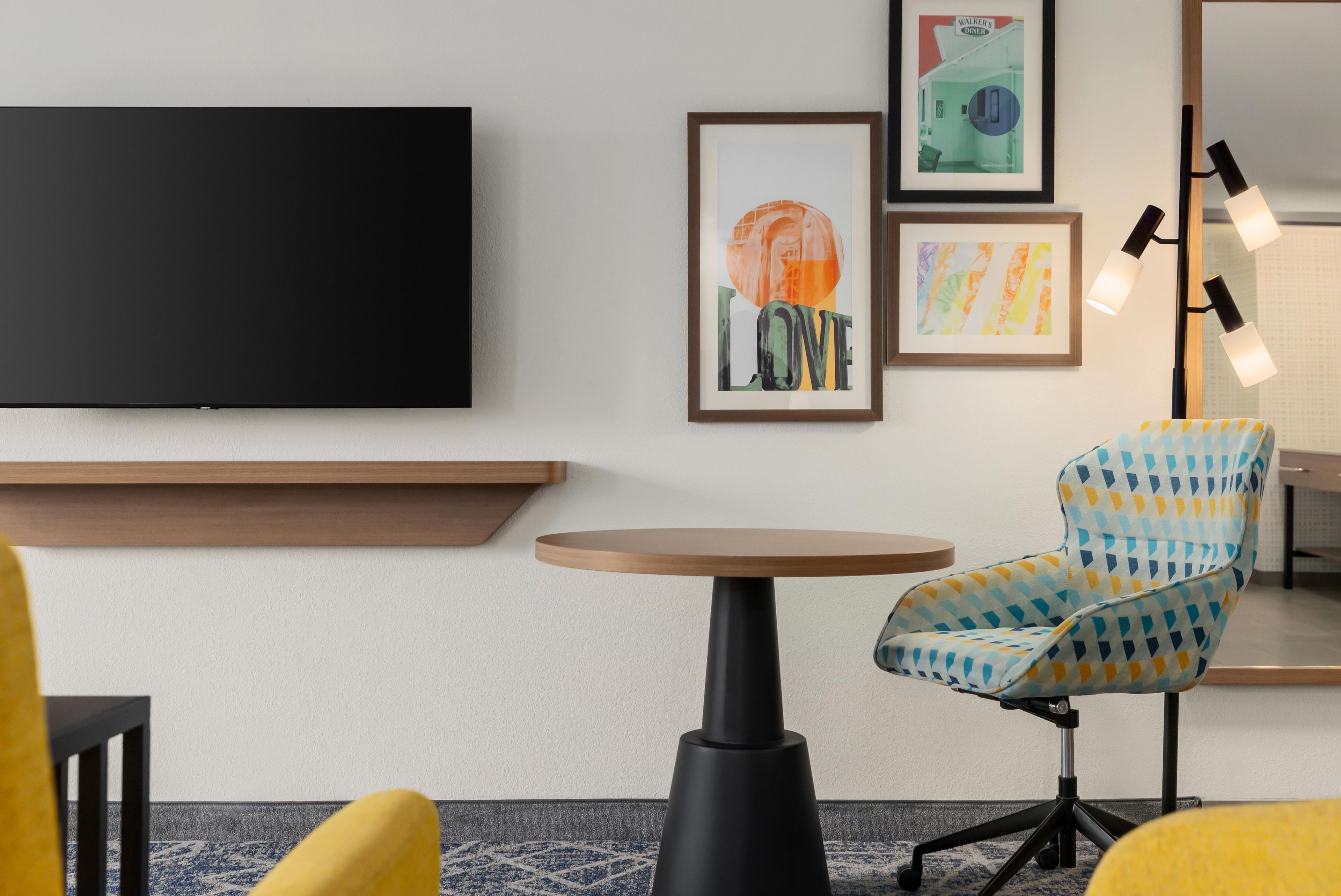 A modern room with a flat-screen TV, a round table, a patterned armchair, and framed artwork on the wall.