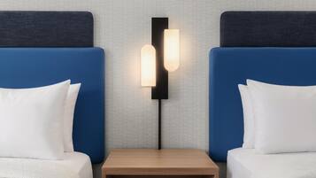 A hotel room with two beds, a nightstand, and a wall-mounted light fixture.