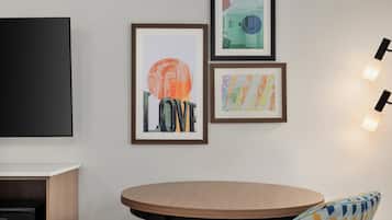A room with a round wooden table, a black TV, and three framed artworks on the wall.