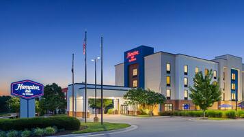 A Hampton Inn by Hilton hotel with a modern design, featuring a prominent sign and flag poles.