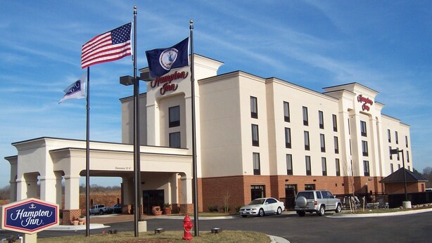 Un hôtel Hampton Inn à la façade blanche, doté de nombreuses fenêtres et surplombant un ciel dégagé.