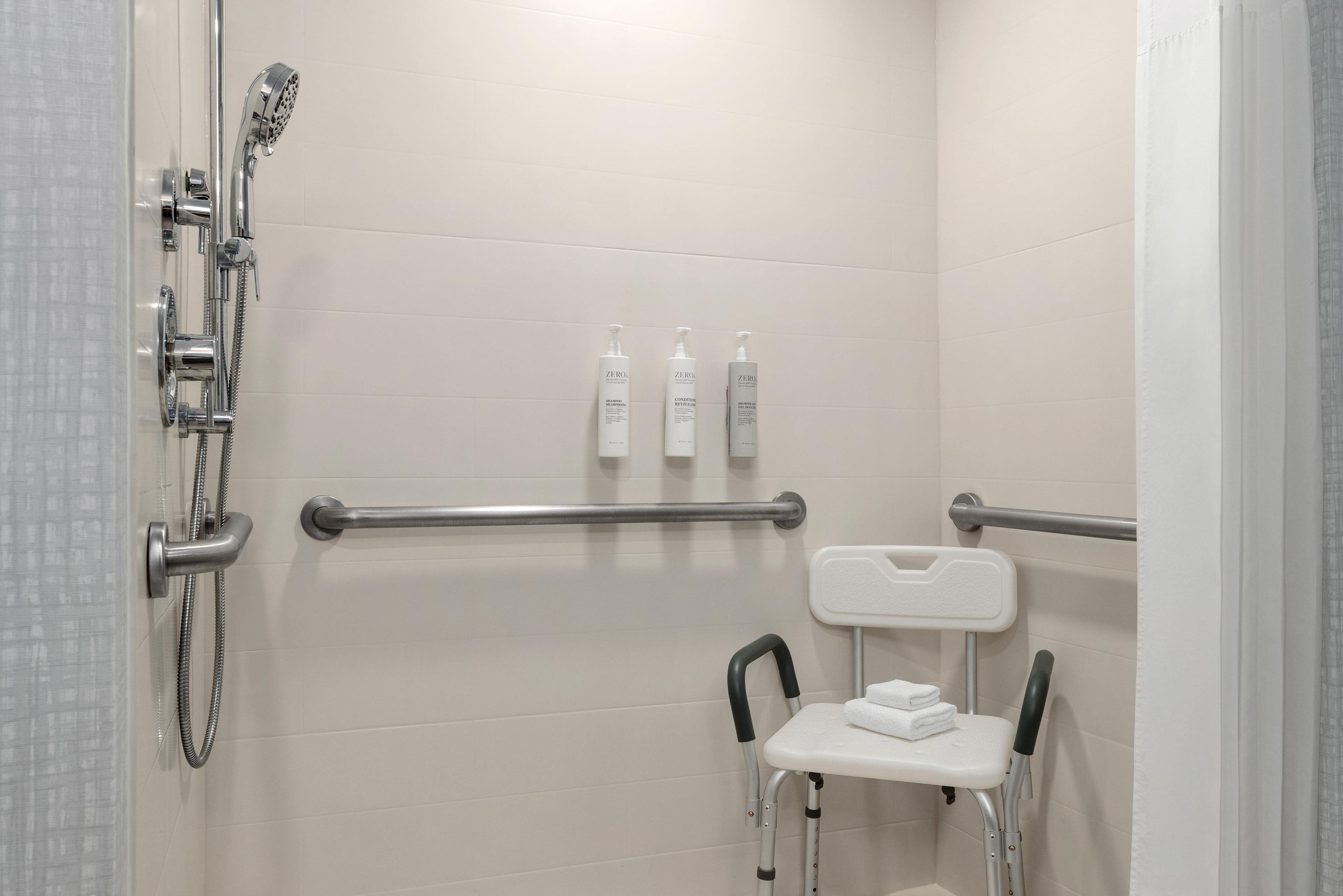 Ein Badezimmer mit Dusche, Haltegriffen, einer rollstuhlgerechten Sitzbank und Pflegeprodukten.