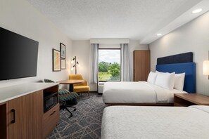 Une chambre d’hôtel avec deux lits, un bureau, une télévision et une fenêtre donnant sur un espace verdoyant.