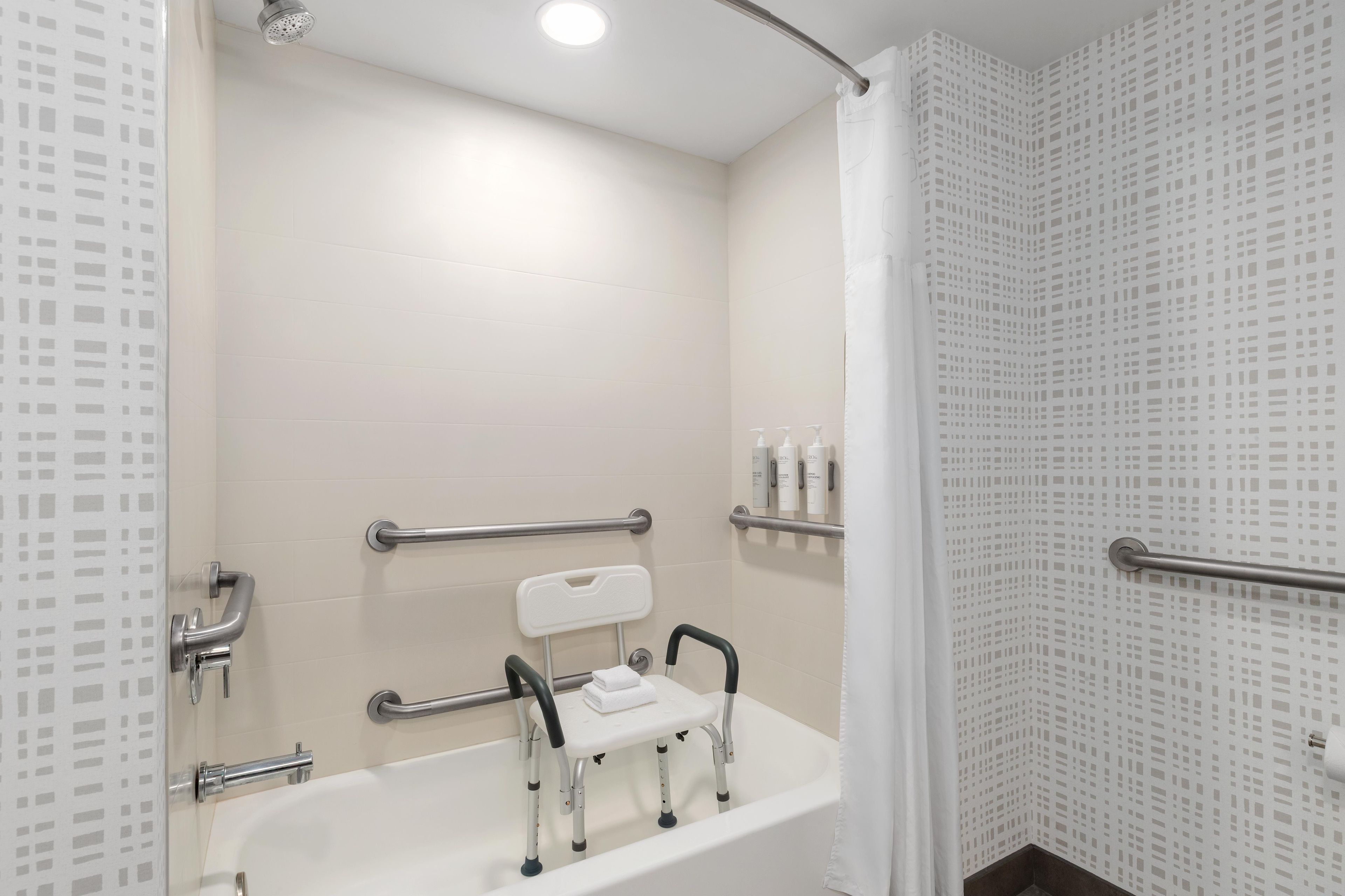 A bathroom with a bathtub, grab bars, a shower curtain, and a handrail.