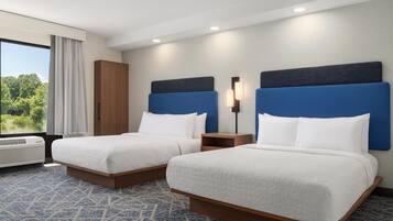 A hotel room with two beds, a wardrobe, a nightstand, and a window with a view of greenery.