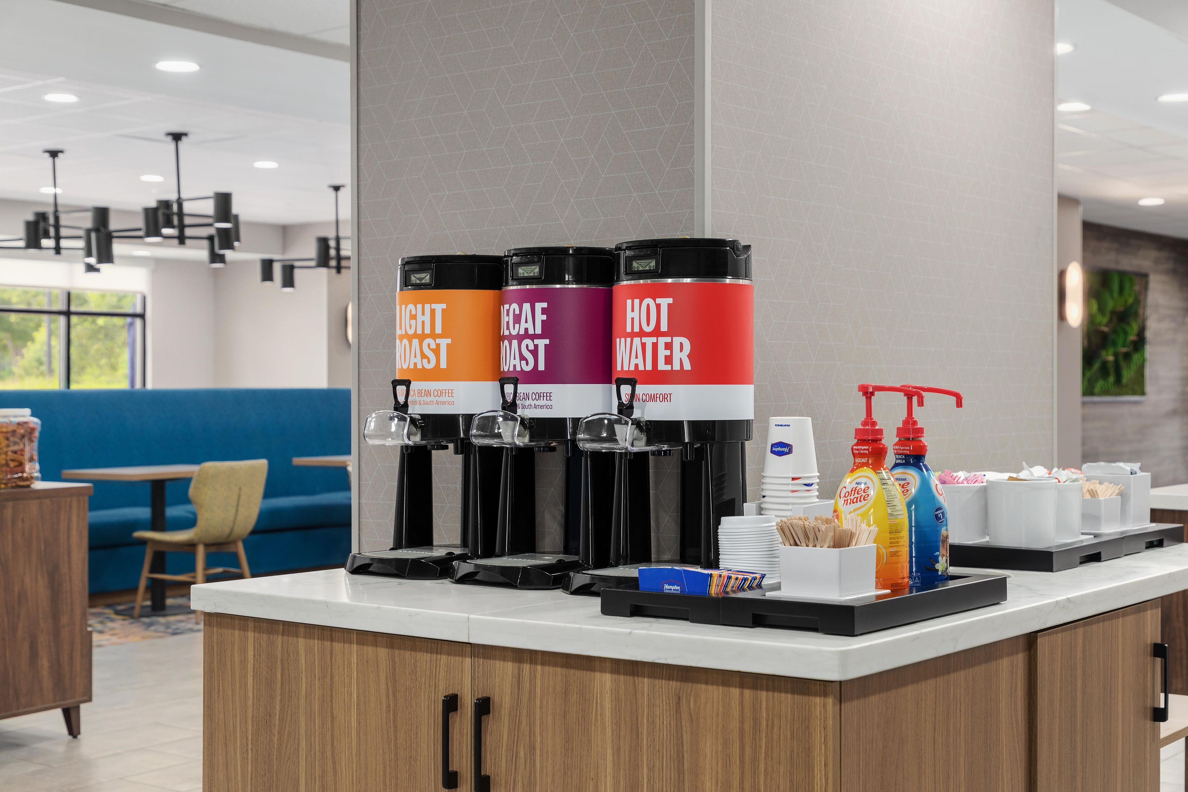 Estación de café con tres dispensadores etiquetados como 'Tueste Suave', 'Tueste Descafeinado' y 'Agua Caliente'.