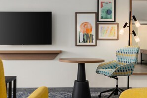 Une chambre moderne dotée d’un téléviseur à écran plat, d’une table ronde, d’un fauteuil à motifs et d’œuvres d’art encadrées accrochées au mur.