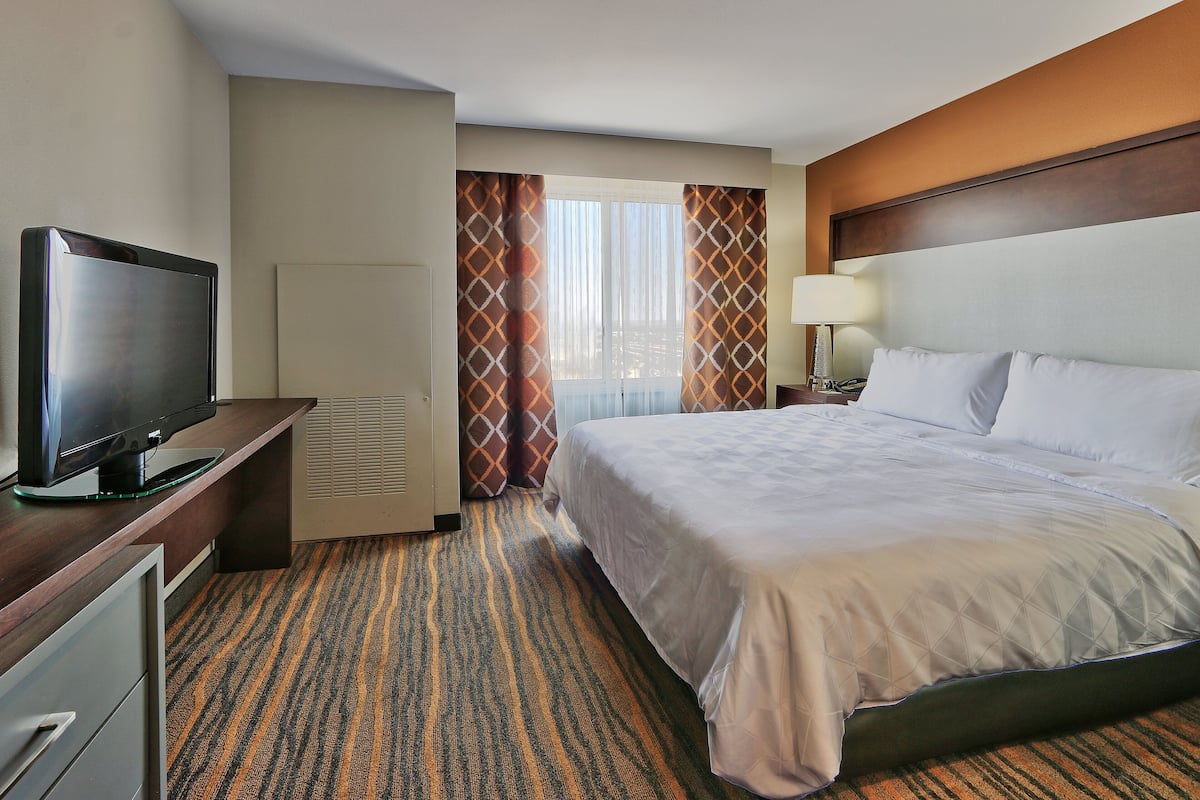 Een hotelkamer met een bed, een televisie, een bureau en een raam met gordijnen.