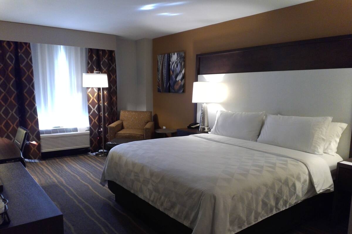Een hotelkamer met een groot bed, een bureau, een stoel, een lamp en een schilderij aan de muur.