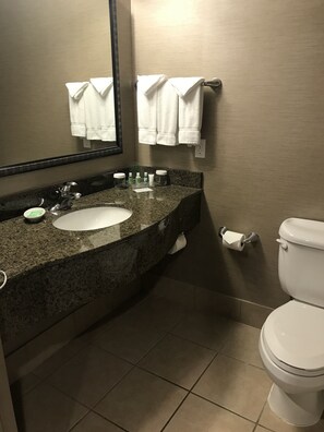 A bathroom with a granite countertop sink, a mirror, a toilet, and two white towels hanging on the wall. - Holiday Inn & Suites Albuquerque-North I-25 by IHG (Albuquerque)