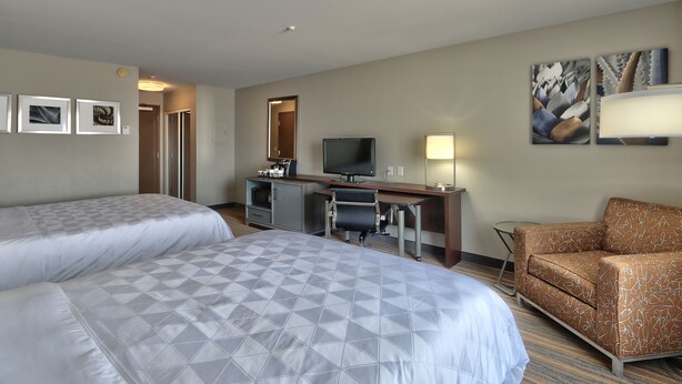 Ein Hotelzimmer mit zwei Betten, einem Schreibtisch mit Computer, einem Stuhl und Bildern an den Wänden.