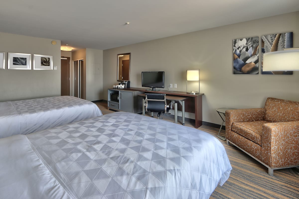 Een hotelkamer met twee bedden, een bureau met een computer, een stoel en kunst aan de muren.