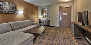 A hotel room with a sofa, a small table, a TV, a desk with a chair, and a carpeted floor. - Holiday Inn & Suites Albuquerque-North I-25 by IHG (Albuquerque)