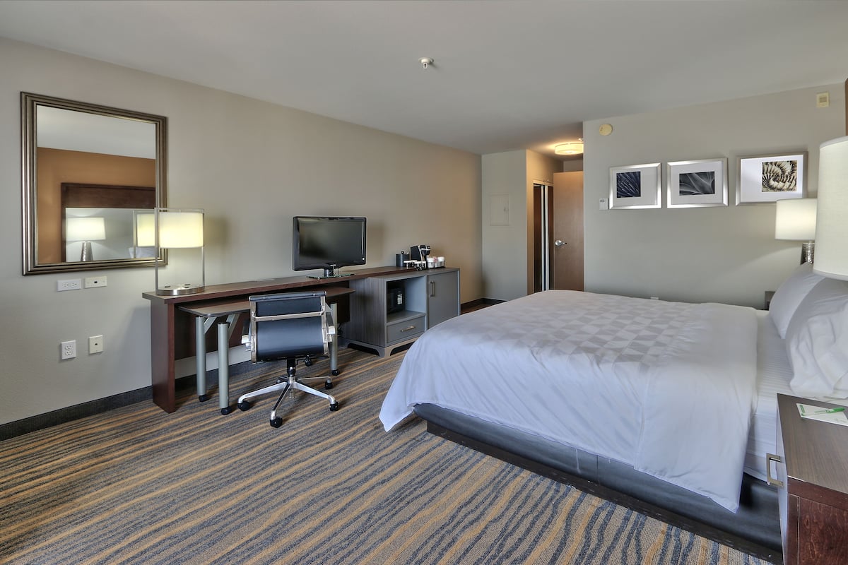 Een hotelkamer met een bed, bureau, stoel, televisie en een kunstwerk aan de muur.