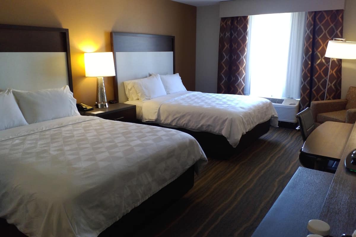 Hotelkamer met twee bedden, een nachtkastje met lamp, een stoel, een bureau met lamp, en een raam met gordijnen.