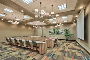 A conference room with a long table, chairs, a projector screen, and a large plant. - Holiday Inn & Suites Albuquerque-North I-25 by IHG (Albuquerque)