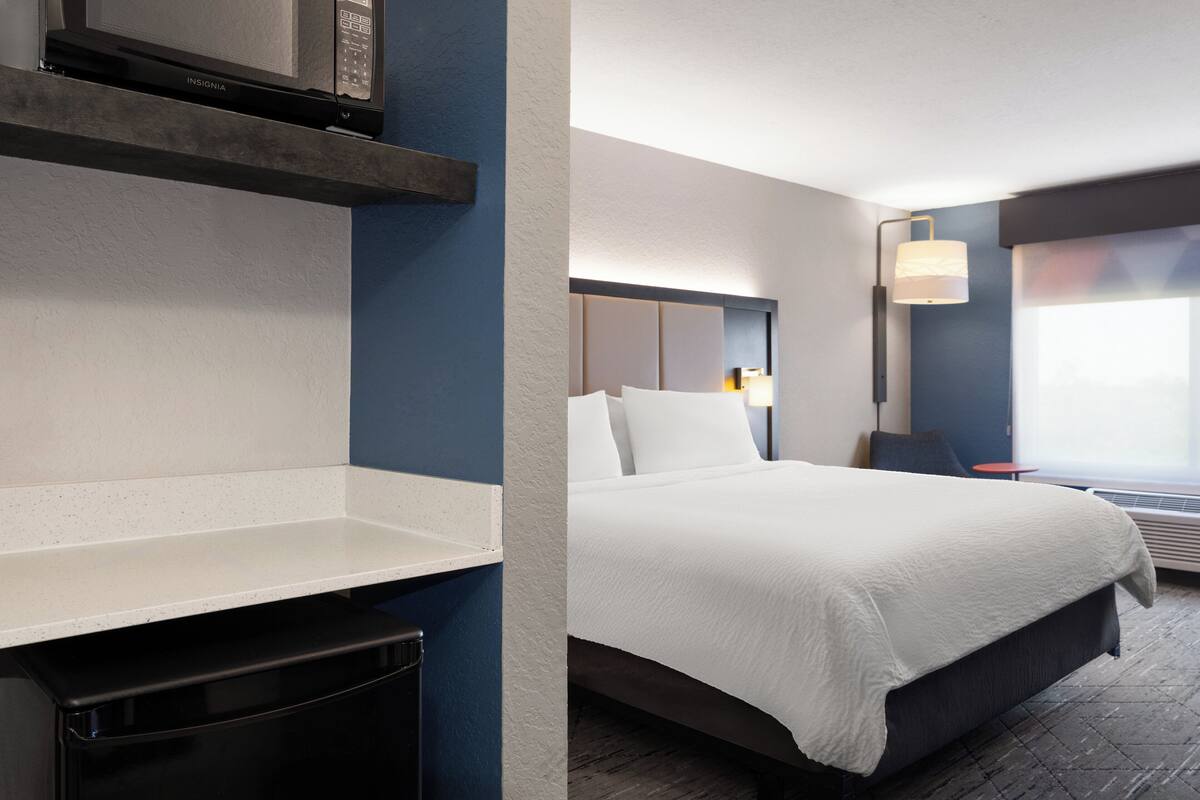 A hotel room with a bed, a nightstand, a lamp, and a window with a view.