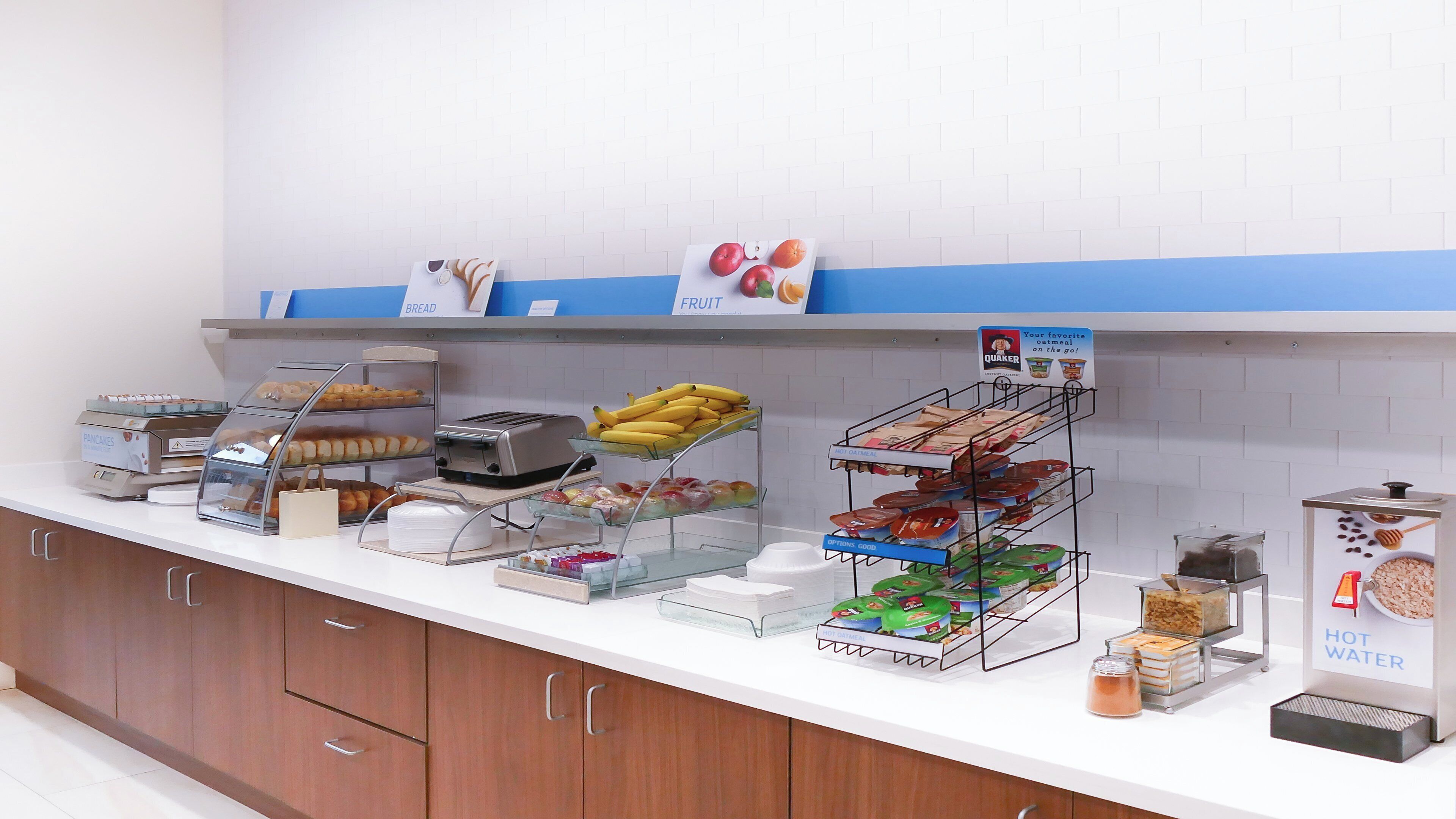 A breakfast buffet with various food options including bread, fruit, and hot water.