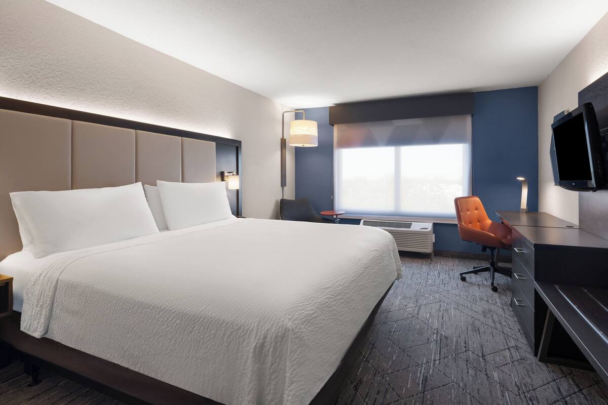 A hotel room with a large bed, a desk with a chair, a TV, and a window with a view.
