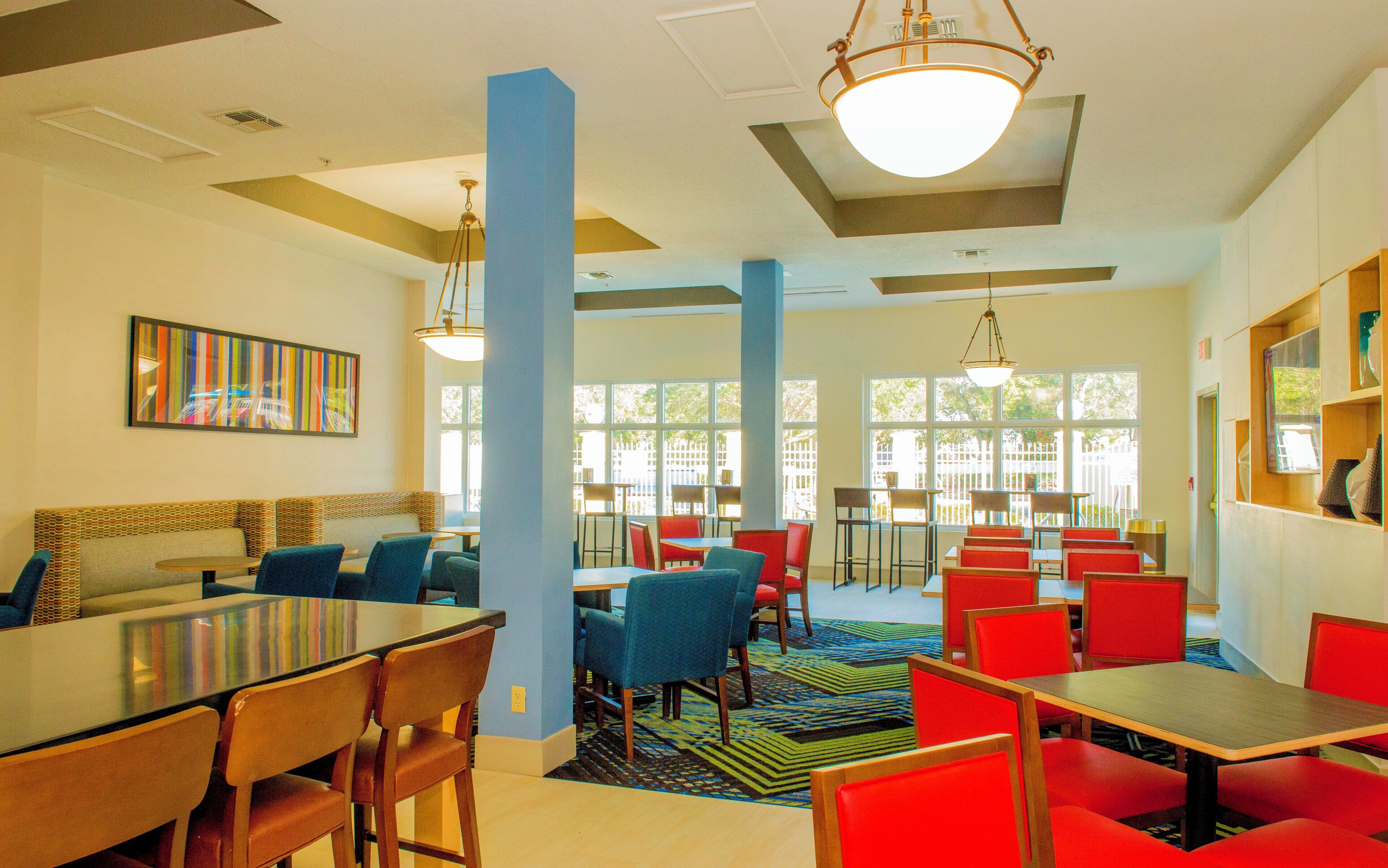A dining area with multiple tables and chairs, large windows, and a ceiling with recessed lighting.