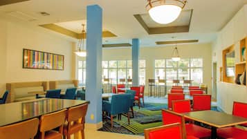 A dining area with multiple tables and chairs, large windows, and a ceiling with recessed lighting.