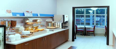 A breakfast bar with various food options, a coffee machine, and a window with a view of the outside.