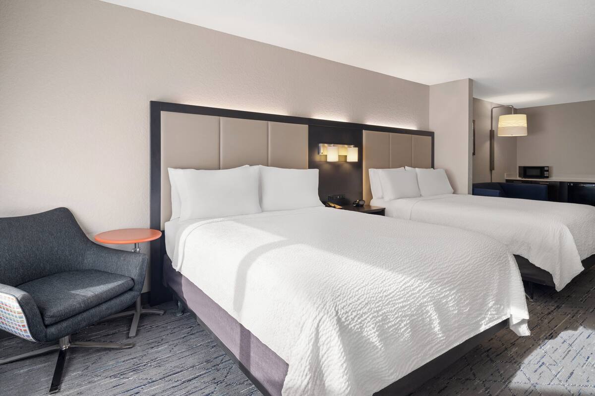 A hotel room with two beds, a small round table, a chair, and a microwave.
